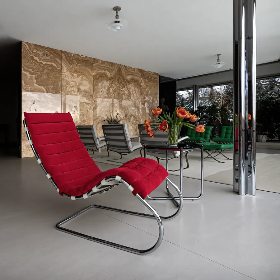 De honingkleurige onyxwand in Villa Tugendhat met een rode lounge stoel ervoor